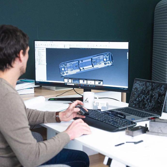 Expert en bureau d'études réalisant sur un ordinateur la modélisation 3D d'une charnière de smartphone pliable en carbone haute performance