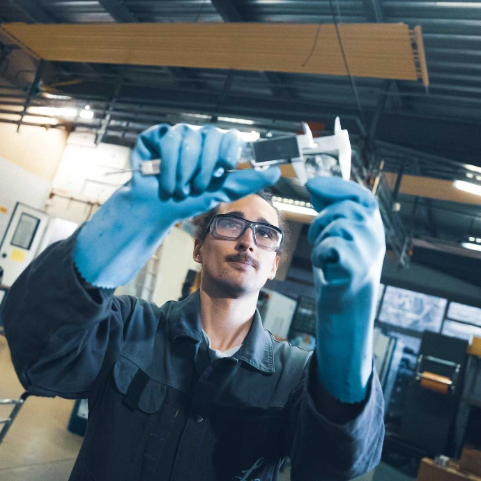 Technicien de face qui réalise un contrôle qualité avec une pièce et l’outil de mesure dans ses mains